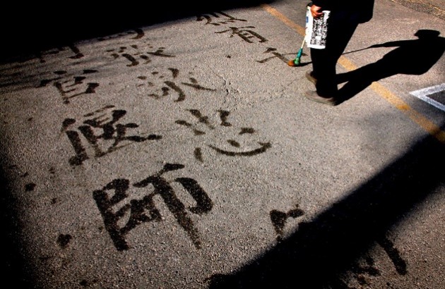 مردی با استفاده از آب و یک برس، بر پیاده­‌رویی در مرکز پکن حروف چینی می‌­نویسد